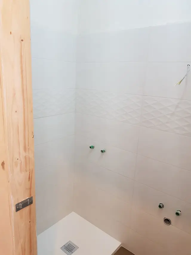 Baie în renovare cu faianță albă și racorduri pregătite pentru obiectele sanitare